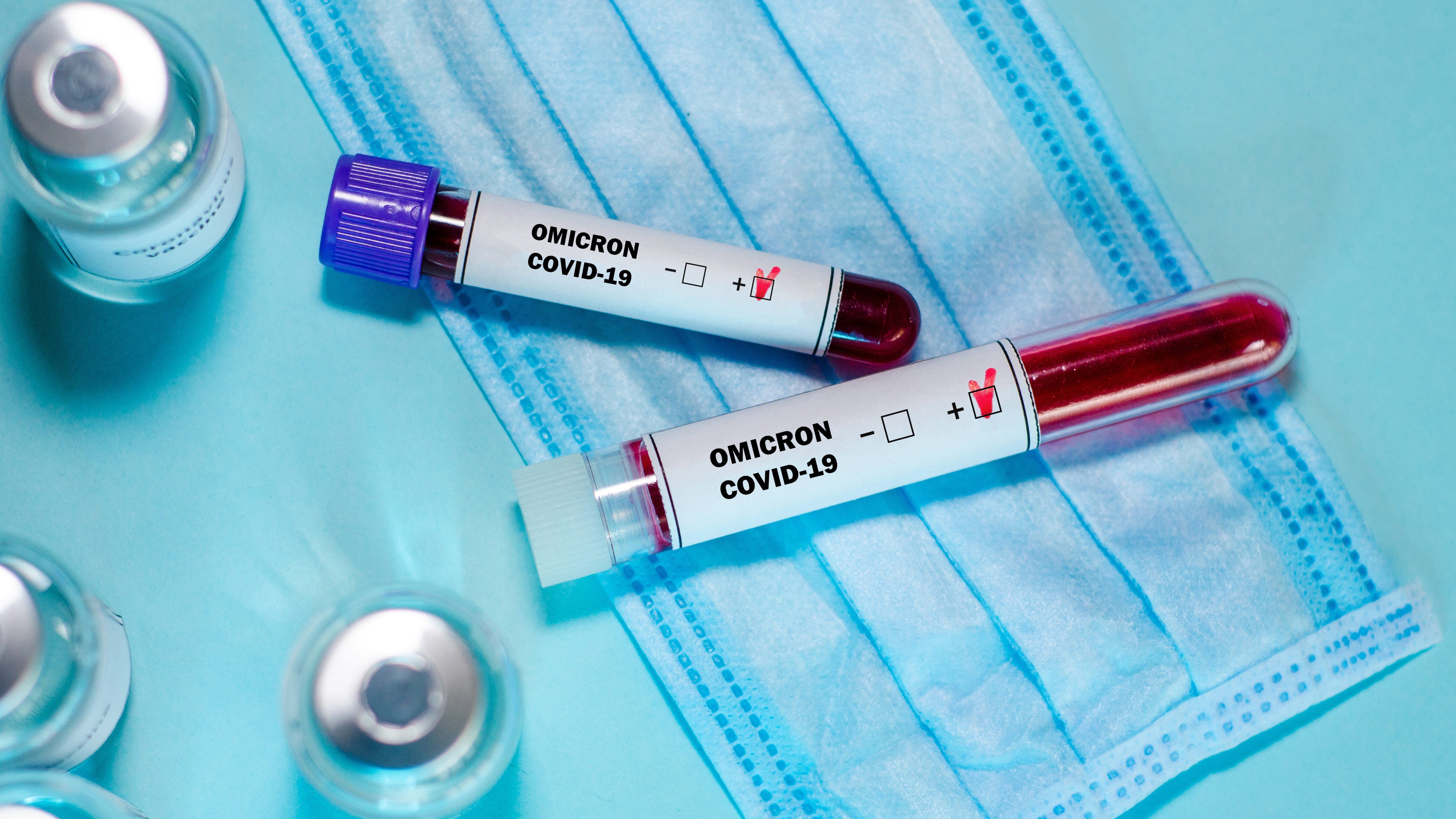 Test tube with positive Omicron COVID-19 test blood sample and vaccine bottle in the medical laboratory.