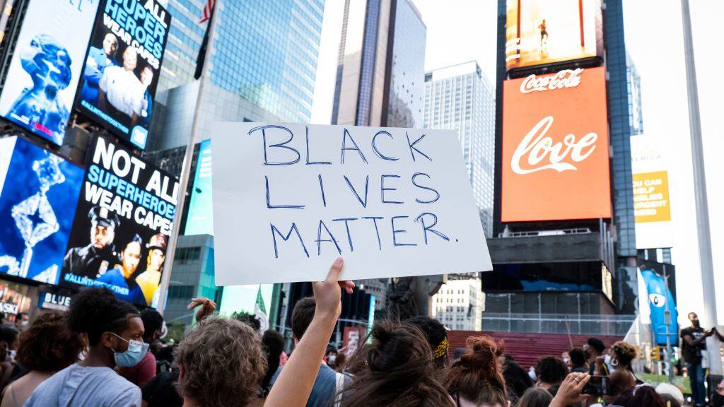 MANHATTAN, NY - July 26: A protester holds a handmade sign that says "Black Lives Matter" with the Coca Cola Jumbotron behind saying the word, "Love" in Father Duffy Square Times Square, New York. This non-violent protest was a March for Black Womxn which started at Times Square and walked through Manhattan. This is days after Portland and other cities have seen federal agents have taken protesters and put into unmarked vehicles while others have been beaten and pepper sprayed. Protesters continue taking to the streets across America and around the world after the killing of George Floyd at the hands of a white police officer Derek Chauvin that was kneeling on his neck during for eight minutes, was caught on video and went viral. During his arrest as Floyd pleaded, "I Can't Breathe". The protest are attempting to give a voice to the need for human rights for African American's and to stop police brutality against people of color. They are also protesting deep-seated racism in America. Many people were wearing masks and observing social distancing due to the coronavirus pandemic. Photographed in the Manhattan Borough of New York on July 26, 2020, USA. (Photo by Ira L. Black/Corbis via Getty Images)