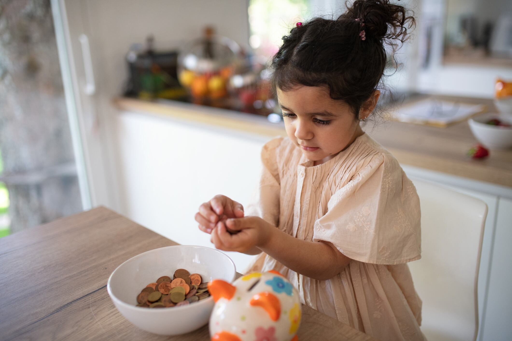 Little multiracial girl saving her money in to porcelain pig.