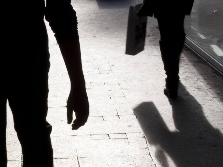 Blurry silhouette and shadow of a woman carrying a bag and a man following her, in the city street in the night