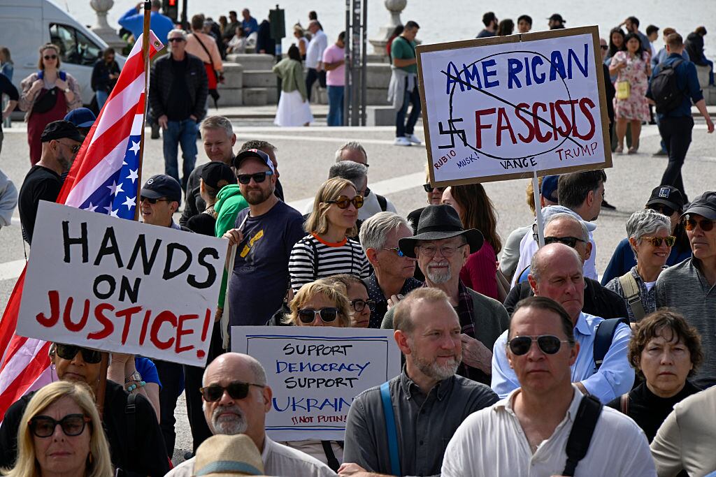LISBON, PORTUGAL - APRIL 05: US residents in Portugal hold placards and a US flag while gathering in Praça do Comercio during a protest organized by American activists living in Portugal, with the common goal of fighting against the political plans of Trump and Elon Musk, and against “the destruction of democratic institutions” in the United States on April 05, 2025, in Lisbon, Portugal. The actions are part of the #HandsOff Day of Action and Solidarity, the demonstration “Lisbon against attacks! Hands off!” in protest against US President Donald Trump and Elon Musk. (Photo by Horacio Villalobos#Corbis/Corbis via Getty Images)