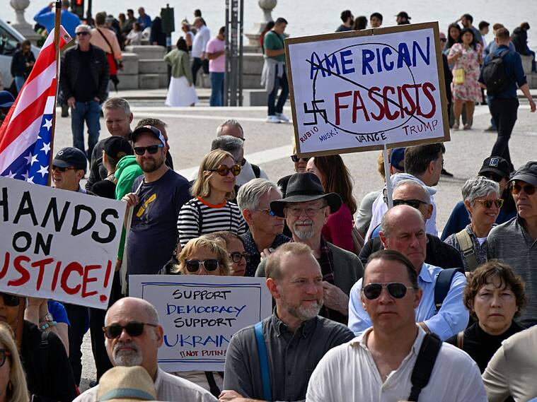 LISBON, PORTUGAL - APRIL 05: US residents in Portugal hold placards and a US flag while gathering in Praça do Comercio during a protest organized by American activists living in Portugal, with the common goal of fighting against the political plans of Trump and Elon Musk, and against “the destruction of democratic institutions” in the United States on April 05, 2025, in Lisbon, Portugal. The actions are part of the #HandsOff Day of Action and Solidarity, the demonstration “Lisbon against attacks! Hands off!” in protest against US President Donald Trump and Elon Musk. (Photo by Horacio Villalobos#Corbis/Corbis via Getty Images)