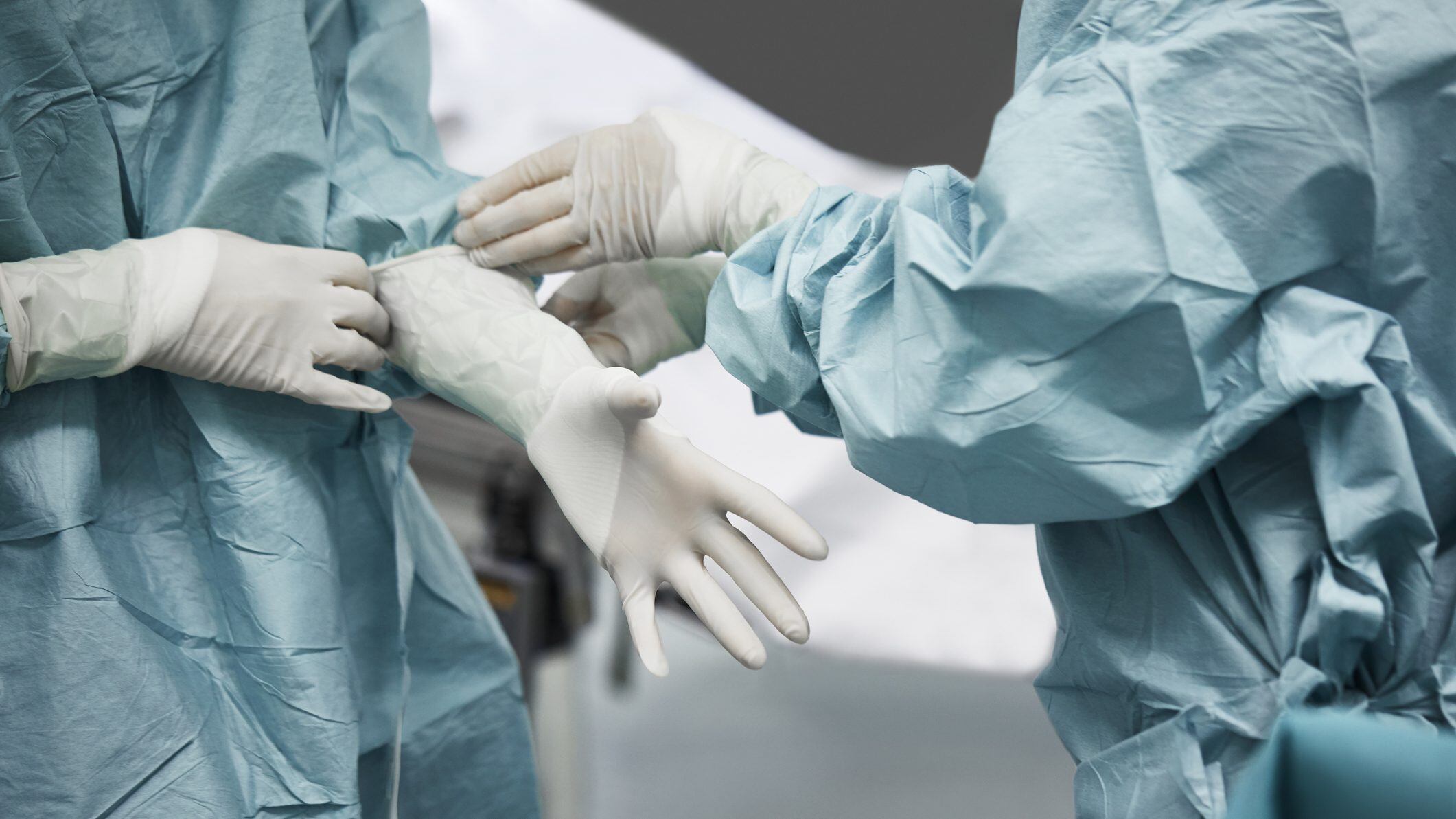 Midsection of female doctor helping surgeon wearing surgical glove. Medical colleagues are preparing for surgery. They are standing in emergency room.
