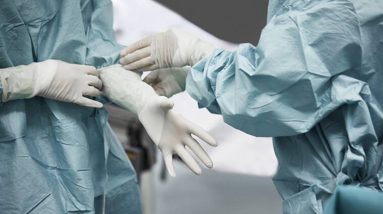 Midsection of female doctor helping surgeon wearing surgical glove. Medical colleagues are preparing for surgery. They are standing in emergency room.