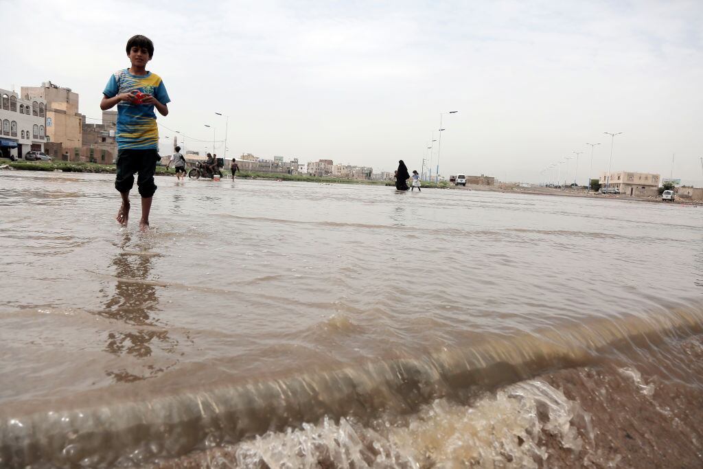Las personas caminan sobre el agua en una zona de la ciudad de Saná en Yemen, luego de las lluvias intensas.