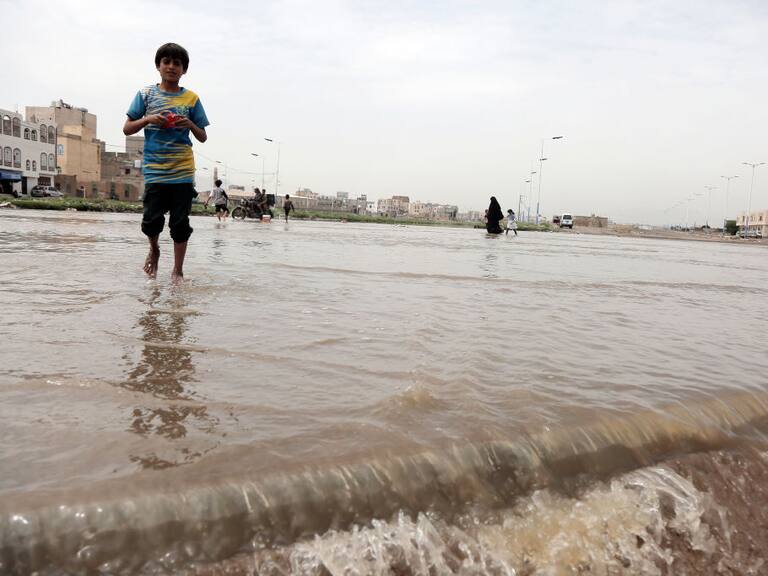 Las personas caminan sobre el agua en una zona de la ciudad de Saná en Yemen, luego de las lluvias intensas.