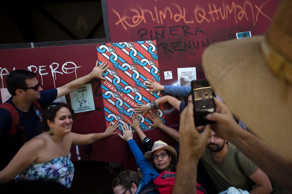 Tourists pose for a picture with a poster that reads "Let's keep united" in Santiago, Chile, on January 10, 2020. - A free walking tour of the "ground zero" of the protests seeks to explain, through street art, the genesis and evolution of the social uprising that has shaken Chile for the last three months. (Photo by CLAUDIO REYES / AFP) (Photo by CLAUDIO REYES/AFP via Getty Images)