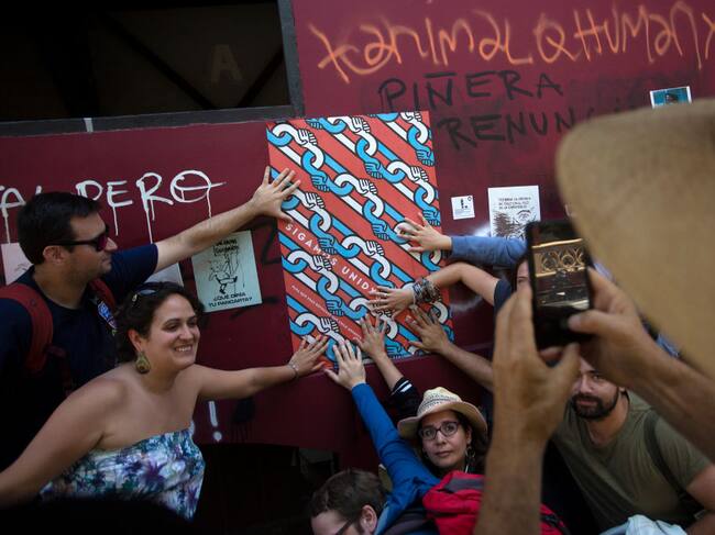 Tourists pose for a picture with a poster that reads "Let's keep united" in Santiago, Chile, on January 10, 2020. - A free walking tour of the "ground zero" of the protests seeks to explain, through street art, the genesis and evolution of the social uprising that has shaken Chile for the last three months. (Photo by CLAUDIO REYES / AFP) (Photo by CLAUDIO REYES/AFP via Getty Images)