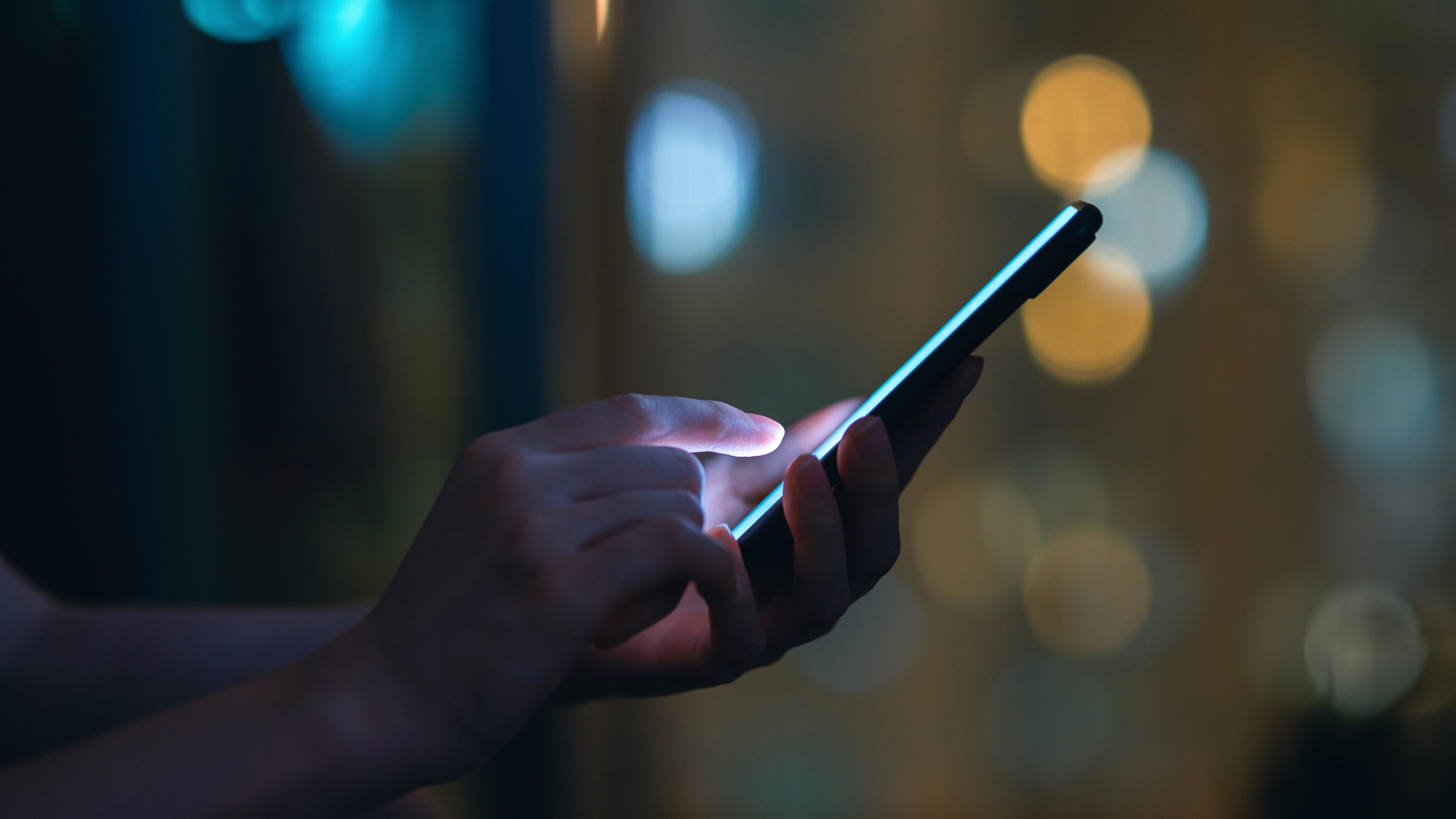 Close up of woman's hand using smartphone in the dark, against illuminated city light bokeh