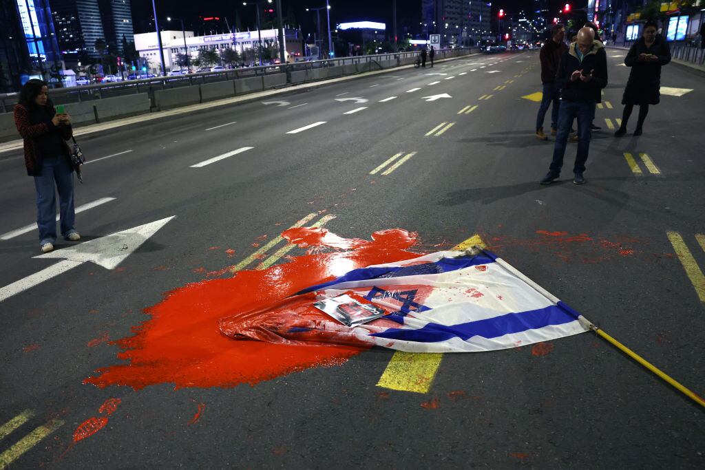 Manifestantes y familias de los rehenes israelíes lanzan una bandera manchada ante el ministerio de defensa de Israel en la ciudad de Tel Aviv