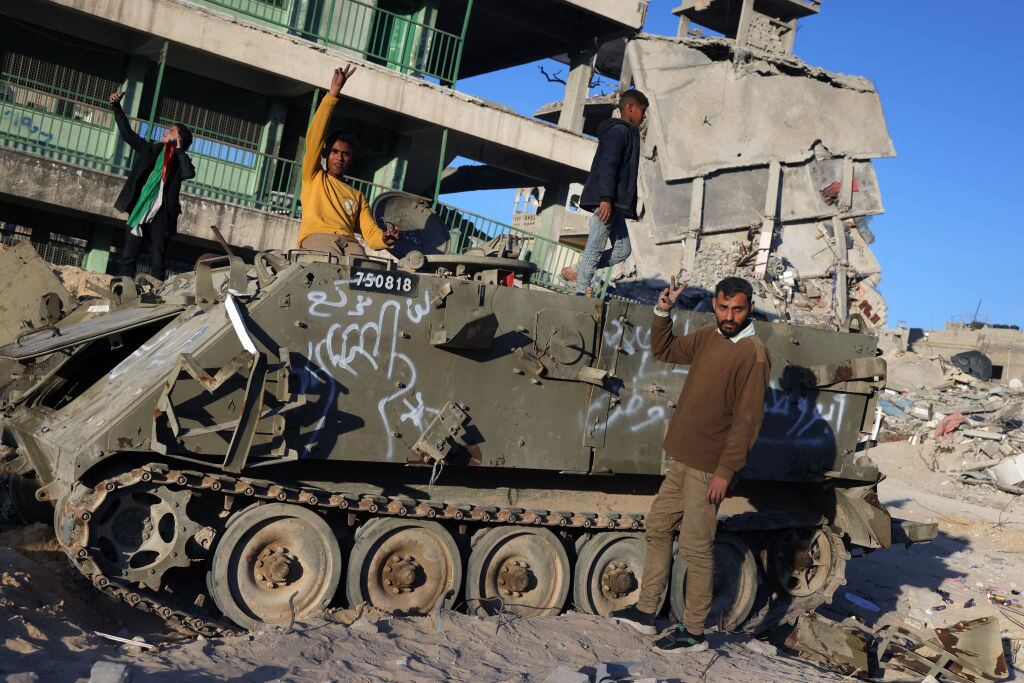 Palestinos posan frente a un tanque israelí destruido en medio de la destrucción que dejaron los ataques militares sobre la Franja de Gaza
