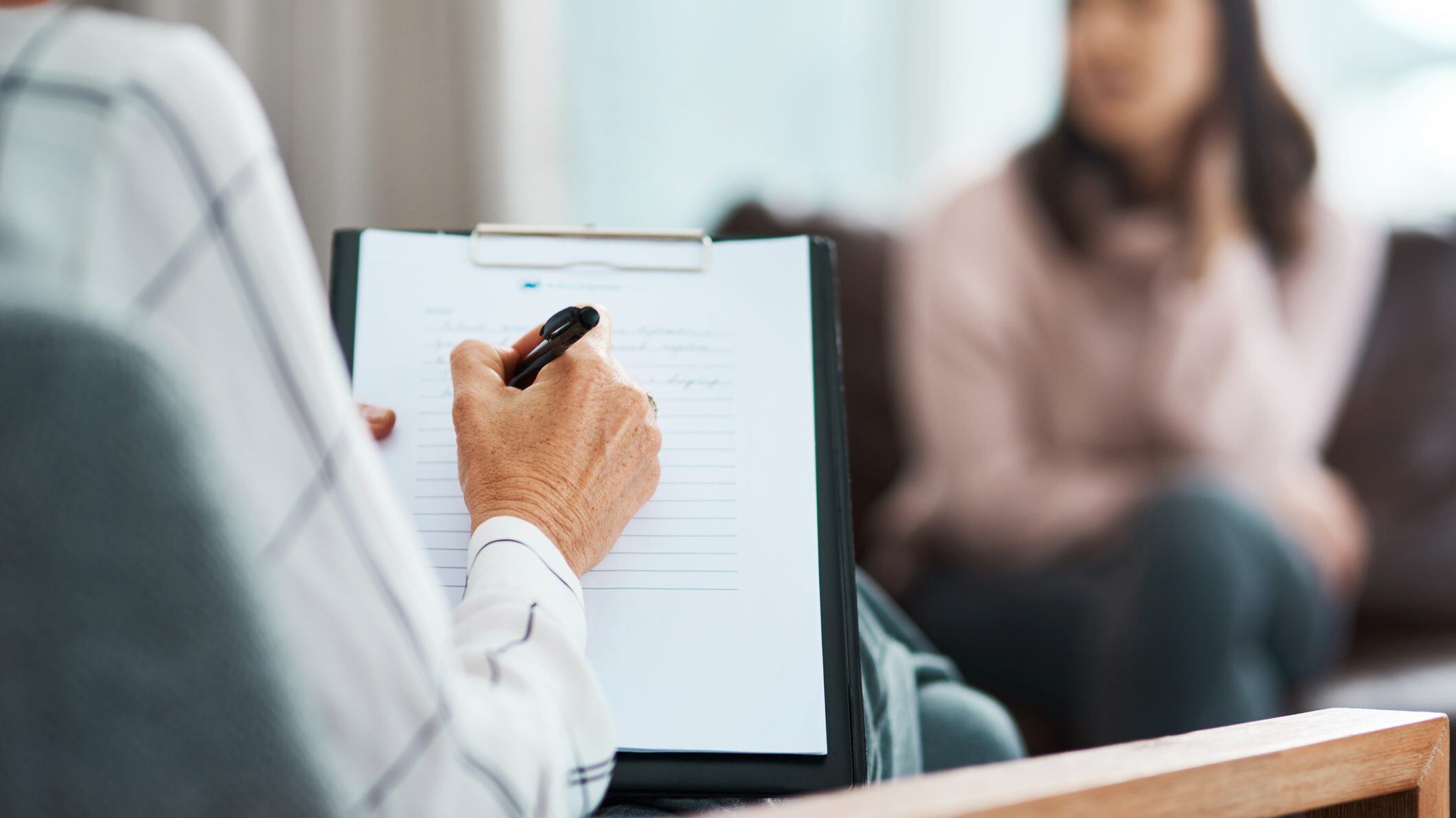 Cropped shot of a psychologist writing notes during a therapeutic session with her patient