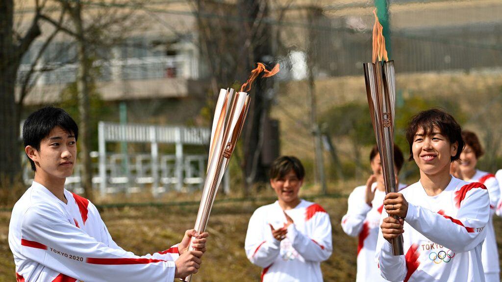 NARAHA, JAPAN - MARCH 25: Torchbearer Azusa Iwashimizu (R), a member of Japan women's national football team, passes the Olympic flame to the high school student Asato Owada at a torch kiss point during the torch relay grand start outside the J Village during the Tokyo Olympic Games torch relay on March 25, 2021 in Naraha, Fukushima, Japan. (Photo by Philip Fong - Pool/Getty Images)