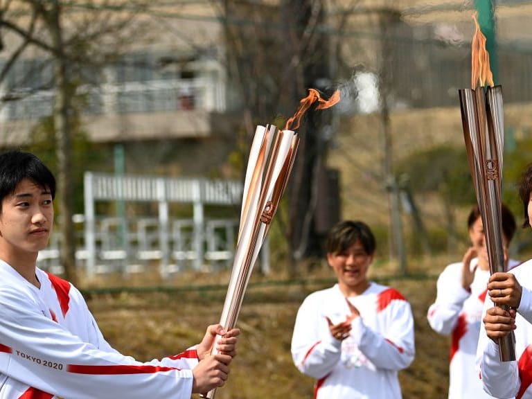 NARAHA, JAPAN - MARCH 25: Torchbearer Azusa Iwashimizu (R), a member of Japan women's national football team, passes the Olympic flame to the high school student Asato Owada at a torch kiss point during the torch relay grand start outside the J Village during the Tokyo Olympic Games torch relay on March 25, 2021 in Naraha, Fukushima, Japan. (Photo by Philip Fong - Pool/Getty Images)
