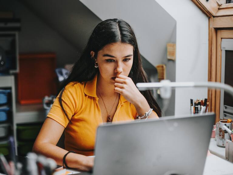 hispanic latina college student works on assignment in her dorm room.She is smiling and in the background there is a big blackboard