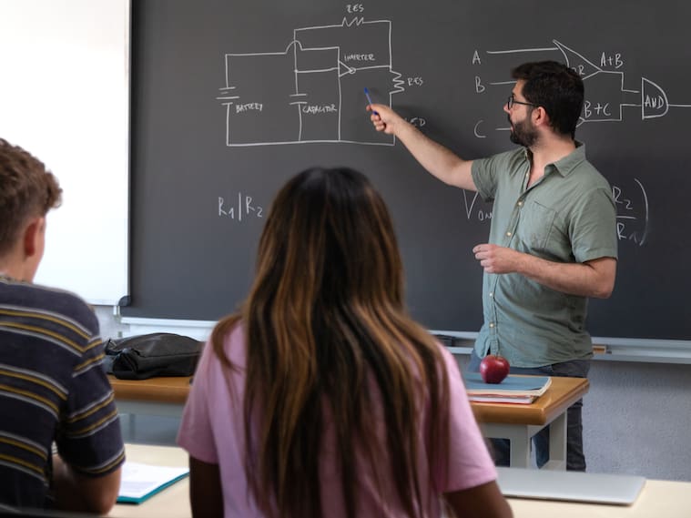 Male caucasian teacher pointing blackboard explaining new concepts to multiracial high school students. Education concept.