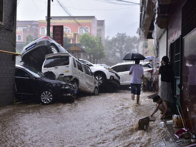 Vehículos acumulados por el agua y las personas que observan la inundación en China