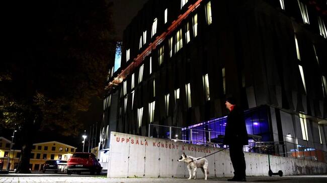 A man holds a dog on the leash at night as he stands in front of the concert hall "Uppsala Konsert & Kongress" in Uppsala, Sweden, on November 2, 2021. - Two people died and one was injured on November 2, 2021 in Sweden's Uppsala after an elderly man fell seven floors, hitting two people, at a concert hall, police said, that was hosting a tribute concert to ABBA legends Bjorn Ulvaeus and Benny Andersson. - Sweden OUT (Photo by Anders WIKLUND / TT News Agency / AFP) / Sweden OUT (Photo by ANDERS WIKLUND/TT News Agency/AFP via Getty Images)
