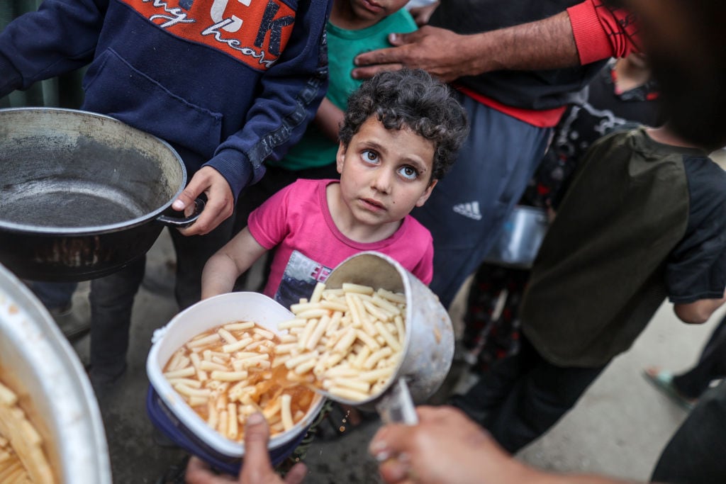 Un niño en la Franja de Gaza espera que le entreguen su plato con comida, en medio de los ataques de Israel.