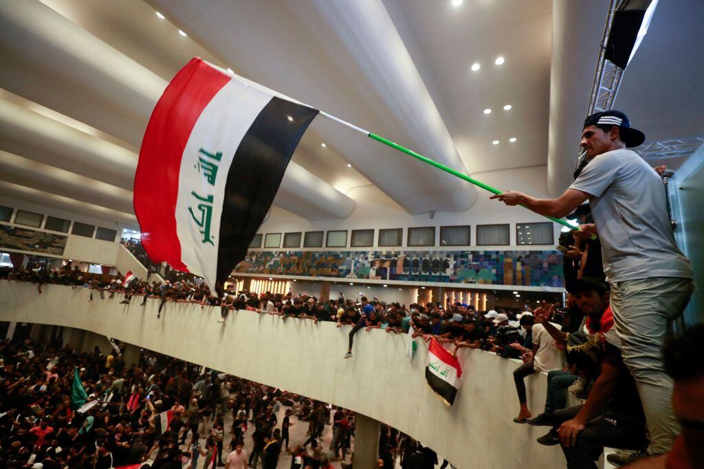 Manifestantes ondean la bandera al interior del parlamento de Irak