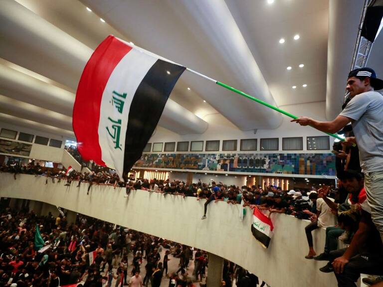 Manifestantes ondean la bandera al interior del parlamento de Irak