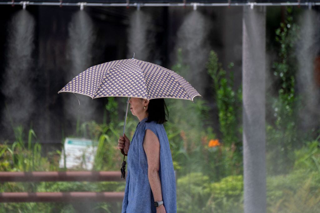 Una mujer camina en Tokio con un paragua cerca de aspersores de agua en medio de la ola de calor que afecta a Japón.