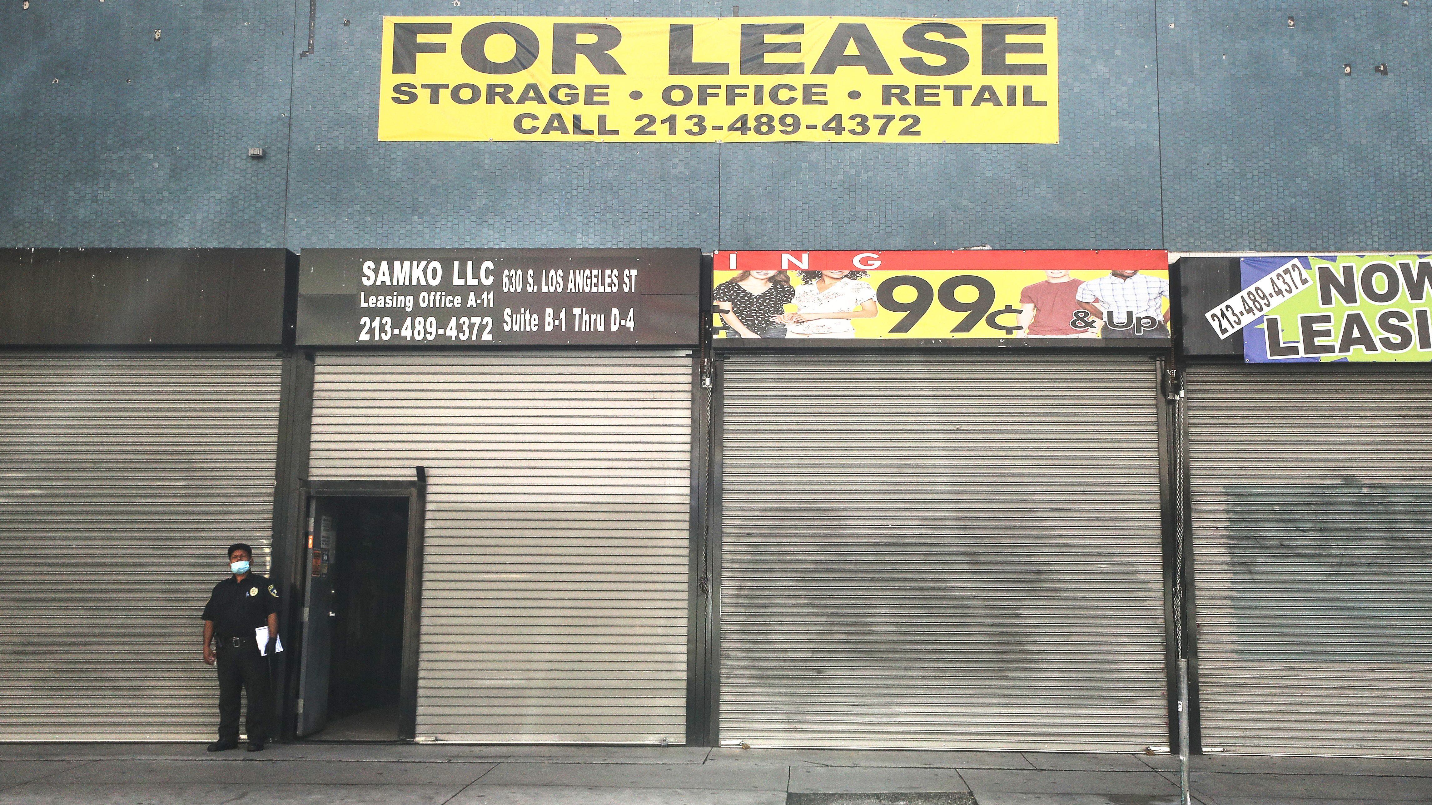 LOS ANGELES, CALIFORNIA - MARCH 30: A security guard wears a face mask while standing outside shuttered shops and a 'For Lease' sign amid the global coronavirus pandemic on March 30, 2020 in Los Angeles, California. The city is planning to set up a field hospital in the Los Angeles Convention Center as a response to an expected surge in COVID-19 patients.  (Photo by Mario Tama/Getty Images)