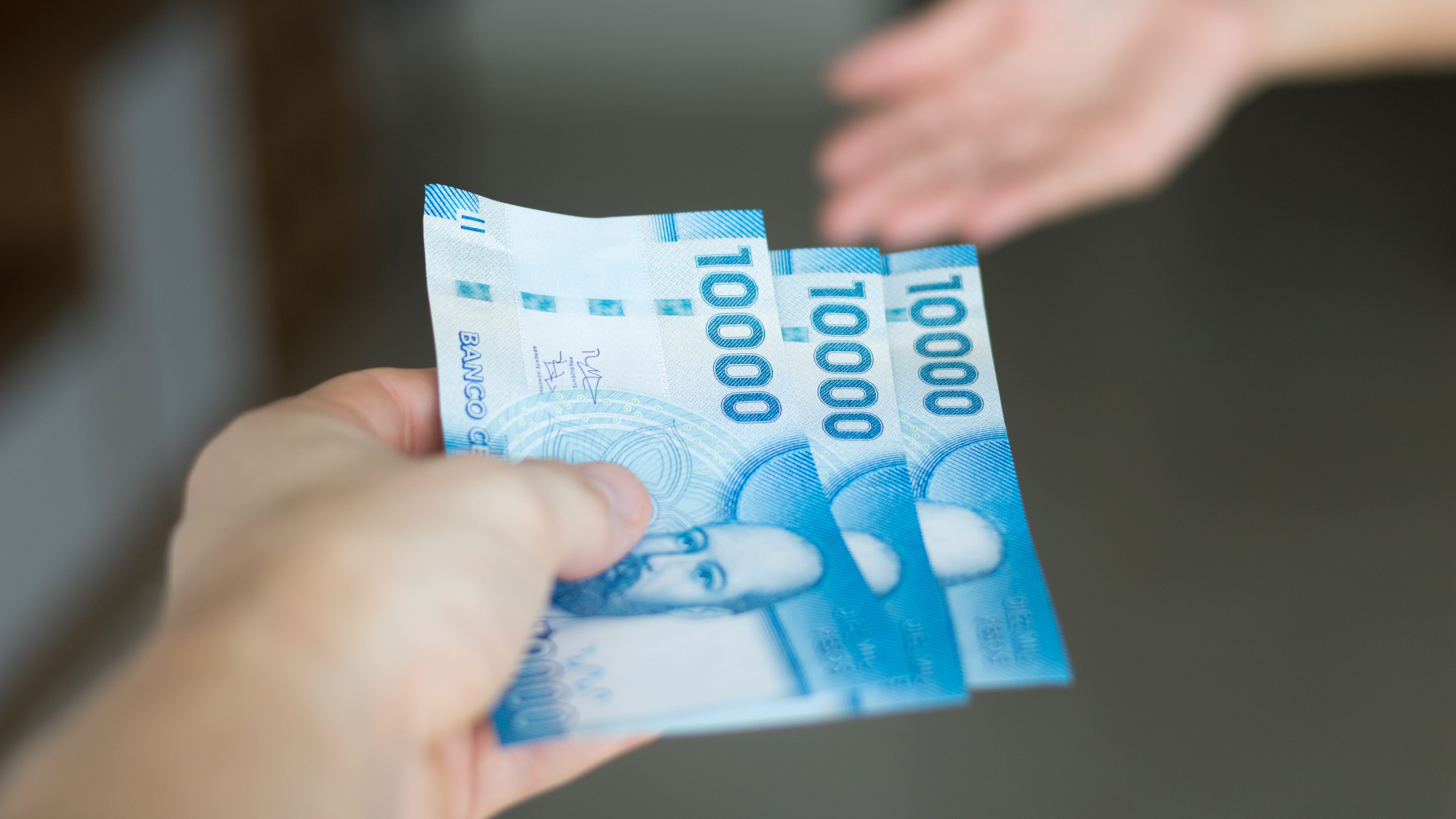 High resolution image. Hands giving and receiving chilean money notes. Chile ten thousand (10000) pesos. Selective focus.