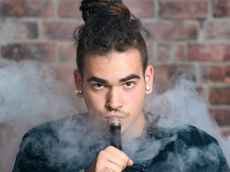 Vaper Smoke outdoor electronic cigarette near the brick wall. Young man smoking big cloud of steam