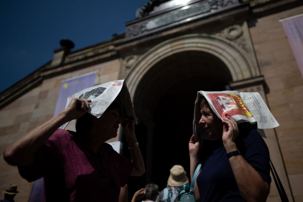 Dos mujeres usan unos periódicos para protegerse de los rayos del sol en la ciudad de Berlín en Alemania.