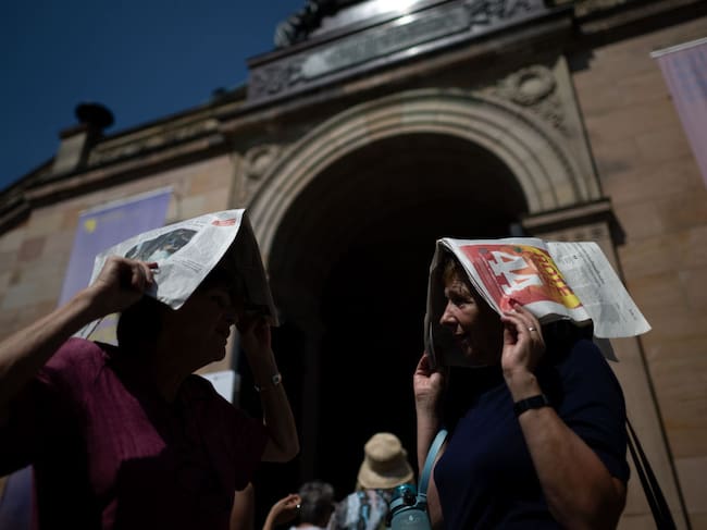 Dos mujeres usan unos periódicos para protegerse de los rayos del sol en la ciudad de Berlín en Alemania.