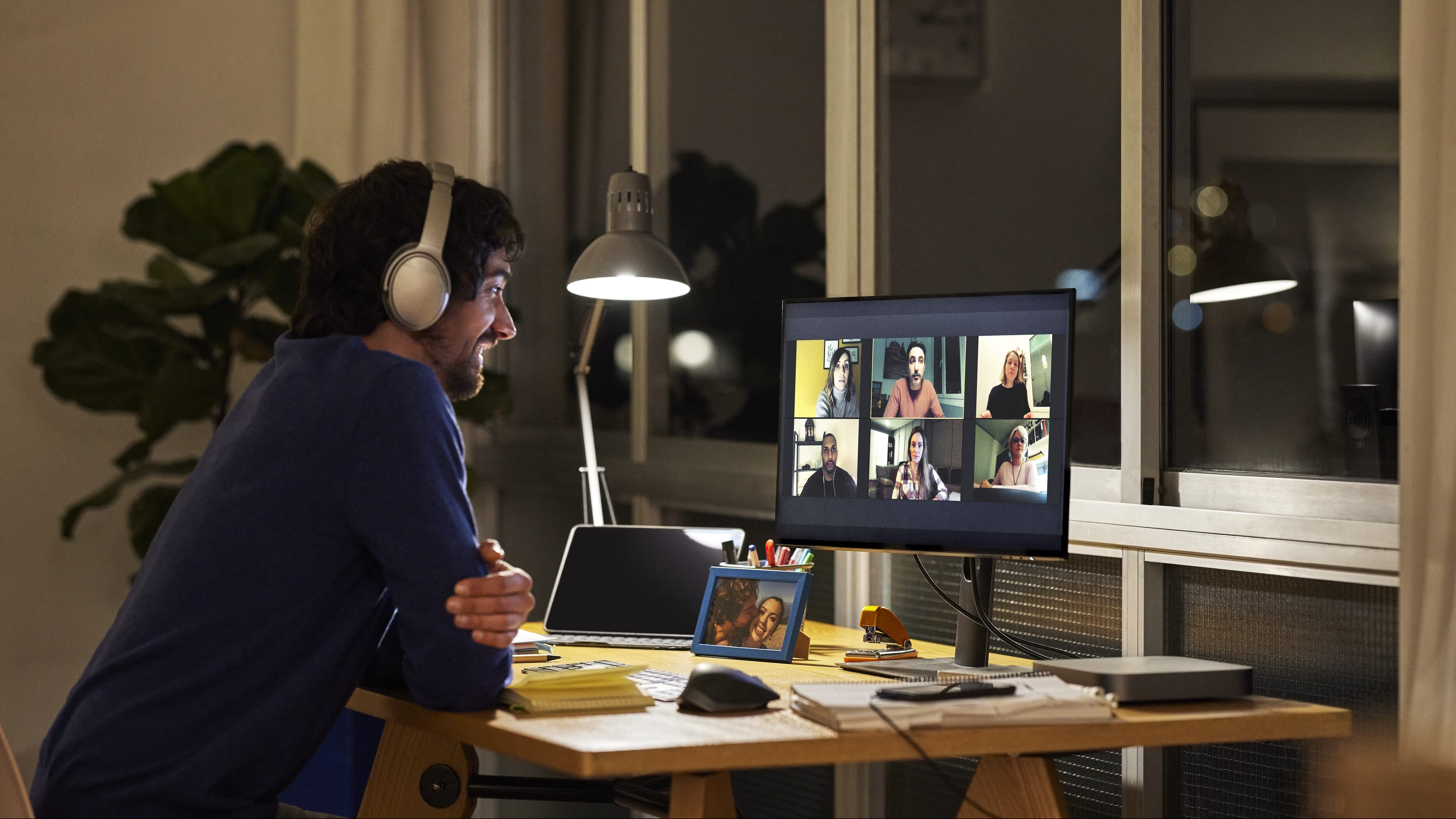 Side view of male freelance worker discussing during video call with colleagues. Smiling businessman is sitting at table in home office. He is working late at night.