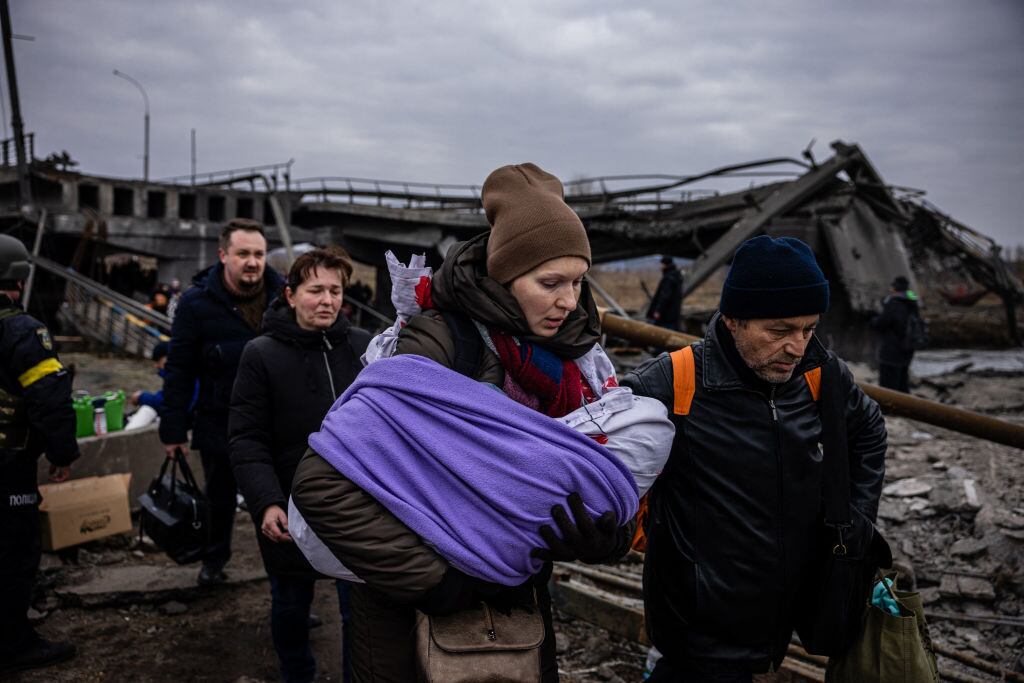 TOPSHOT - A woman carrying her baby crosses a destroyed bridge as they flee the city of Irpin, northwest of Kyiv, on March 7, 2022. - Ukraine dismissed Moscow's offer to set up humanitarian corridors from several bombarded cities on Monday after it emerged some routes would lead refugees into Russia or Belarus. The Russian proposal of safe passage from Kharkiv, Kyiv, Mariupol and Sumy had come after terrified Ukrainian civilians came under fire in previous ceasefire attempts. (Photo by Dimitar DILKOFF / AFP) (Photo by DIMITAR DILKOFF/AFP via Getty Images)