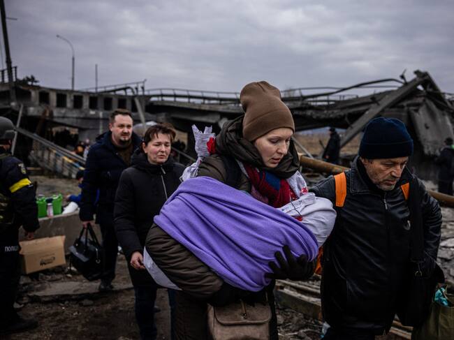 TOPSHOT - A woman carrying her baby crosses a destroyed bridge as they flee the city of Irpin, northwest of Kyiv, on March 7, 2022. - Ukraine dismissed Moscow's offer to set up humanitarian corridors from several bombarded cities on Monday after it emerged some routes would lead refugees into Russia or Belarus. The Russian proposal of safe passage from Kharkiv, Kyiv, Mariupol and Sumy had come after terrified Ukrainian civilians came under fire in previous ceasefire attempts. (Photo by Dimitar DILKOFF / AFP) (Photo by DIMITAR DILKOFF/AFP via Getty Images)