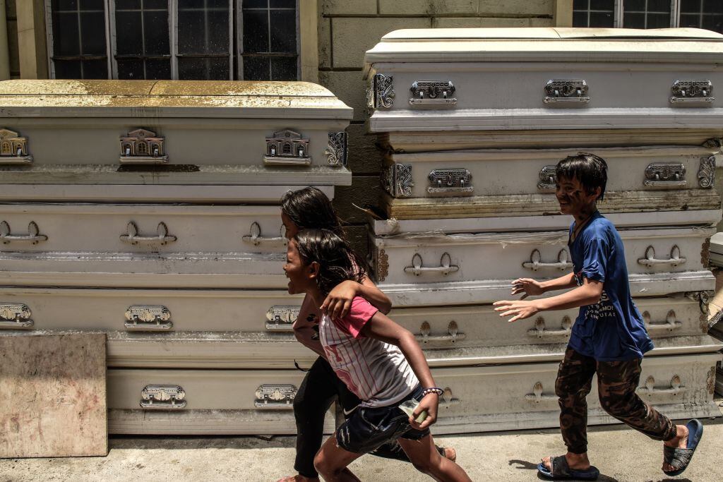 Unos niños corren por al lado de un grupo de féretros en Filipinas