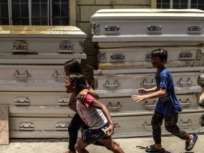 Unos niños corren por al lado de un grupo de féretros en Filipinas
