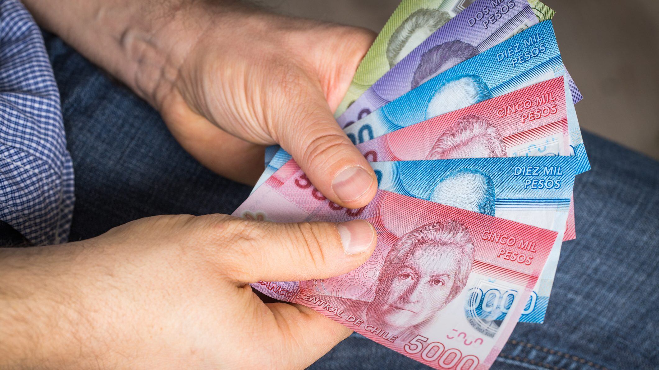 a man holding Chilean money in his hand, Pesos of various values