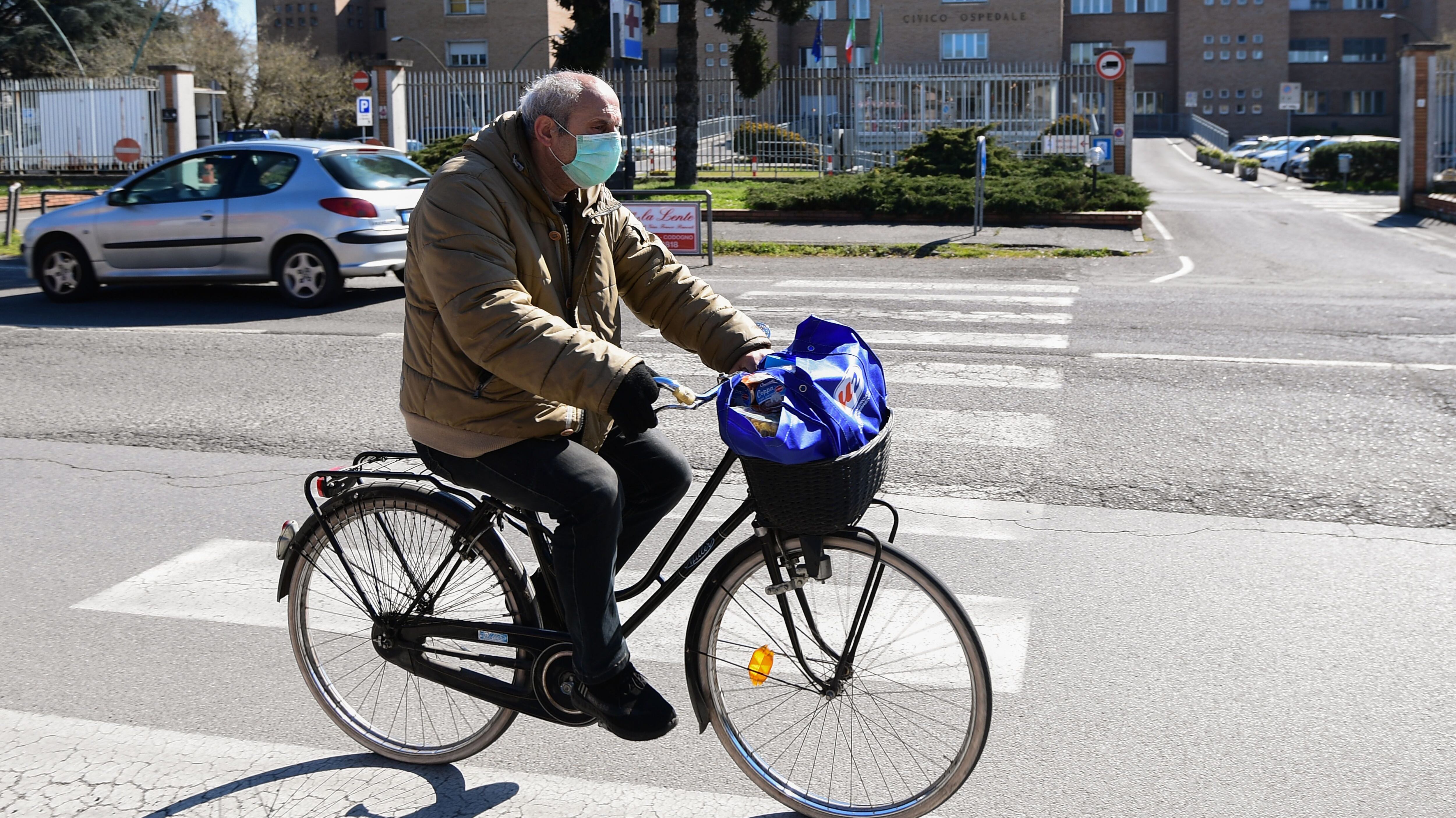 A man wearing a protective mask rides his bicycle past the hospital in Codogno, southeast of Milan, on March 11, 2020 a day after Italy imposed unprecedented national restrictions on its 60 million people Tuesday to control the deadly COVID-19 coronavirus. (Photo by Miguel MEDINA / AFP) (Photo by MIGUEL MEDINA/AFP via Getty Images)