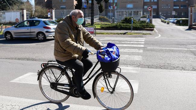 A man wearing a protective mask rides his bicycle past the hospital in Codogno, southeast of Milan, on March 11, 2020 a day after Italy imposed unprecedented national restrictions on its 60 million people Tuesday to control the deadly COVID-19 coronavirus. (Photo by Miguel MEDINA / AFP) (Photo by MIGUEL MEDINA/AFP via Getty Images)