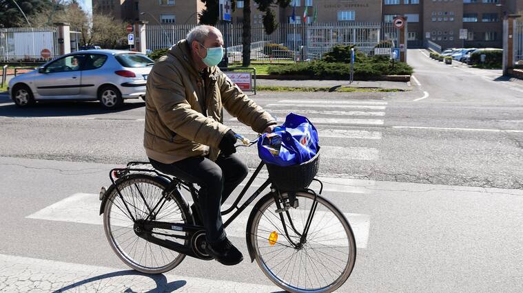 A man wearing a protective mask rides his bicycle past the hospital in Codogno, southeast of Milan, on March 11, 2020 a day after Italy imposed unprecedented national restrictions on its 60 million people Tuesday to control the deadly COVID-19 coronavirus. (Photo by Miguel MEDINA / AFP) (Photo by MIGUEL MEDINA/AFP via Getty Images)
