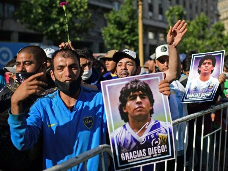 Fans hold photos of Argentinian late football legend Diego Armando Maradona outside the Casa Rosada government house as they wait to pay their tribute to his coffin in Buenos Aires, on November 26, 2020. - Argentine football legend Diego Maradona will be buried Thursday on the outskirts of Buenos Aires, a spokesman said. Maradona, who died of a heart attack Wednesday at the age of 60, will be laid to rest in the Jardin de Paz cemetery, where his parents were also buried, Sebastian Sanchi told AFP. (Photo by RONALDO SCHEMIDT / AFP) (Photo by RONALDO SCHEMIDT/AFP via Getty Images)