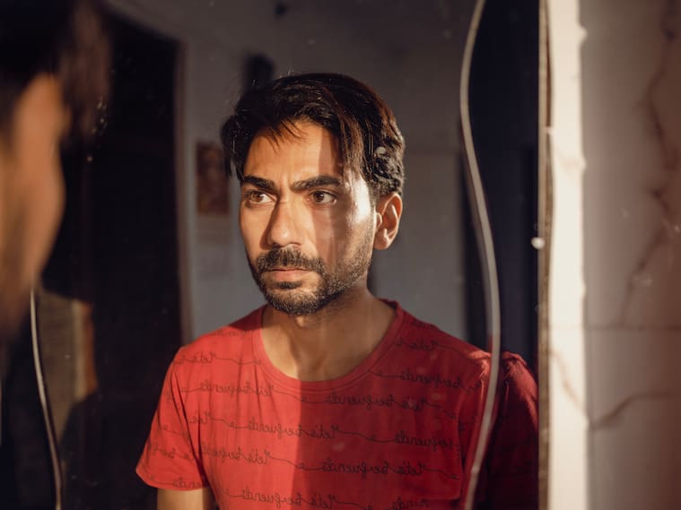 Closeup shot of a man in stress staring in mirror while sunlight falls on his face.