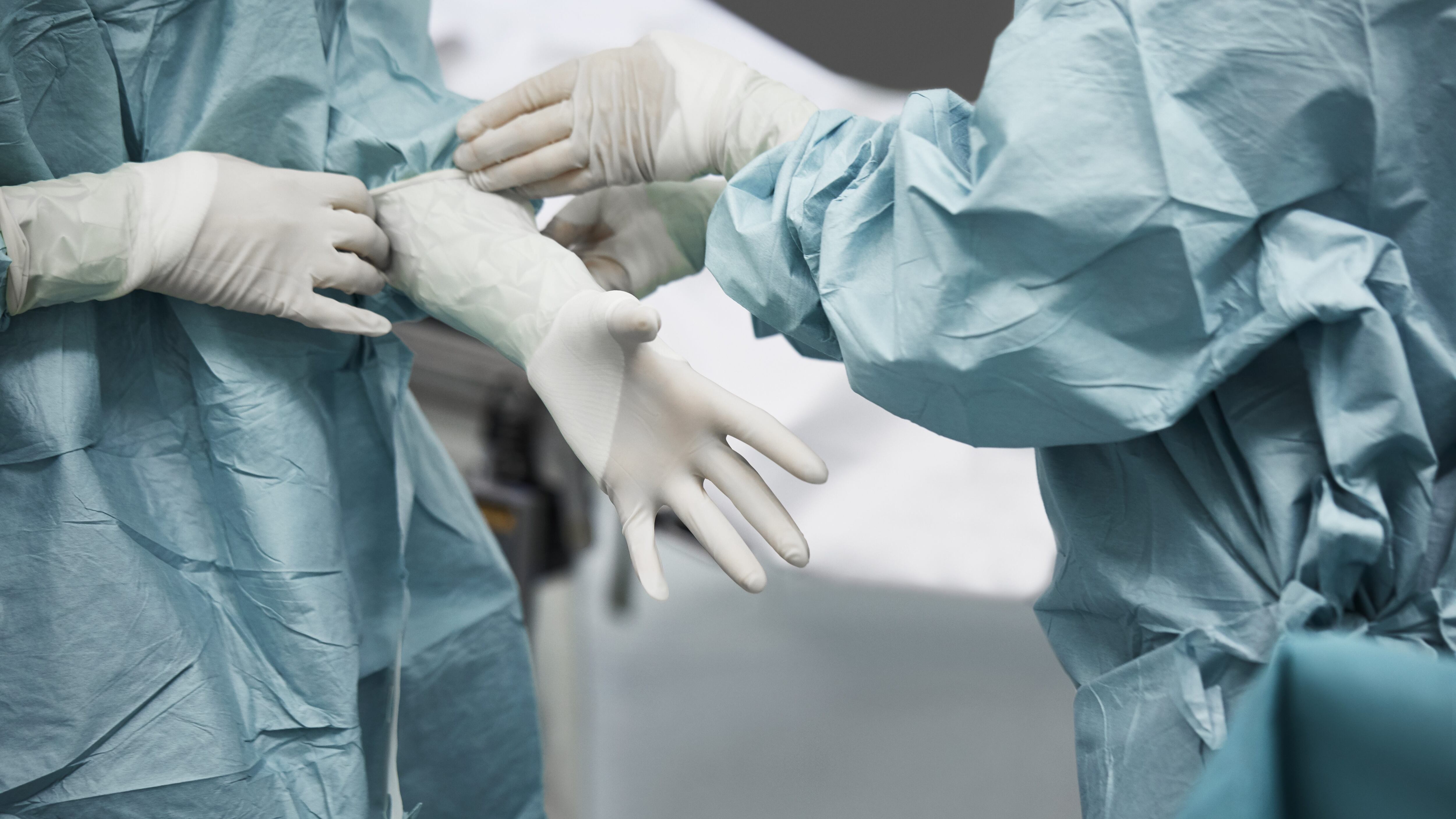 Midsection of female doctor helping surgeon wearing surgical glove. Medical colleagues are preparing for surgery. They are standing in emergency room.