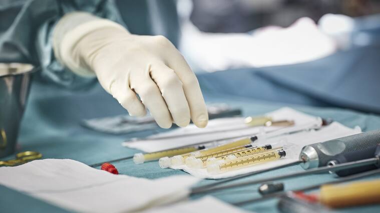Cropped image of female surgeon reaching for syringes on table. Close-up of healthcare worker's hand wearing surgical glove. She is in emergency room.