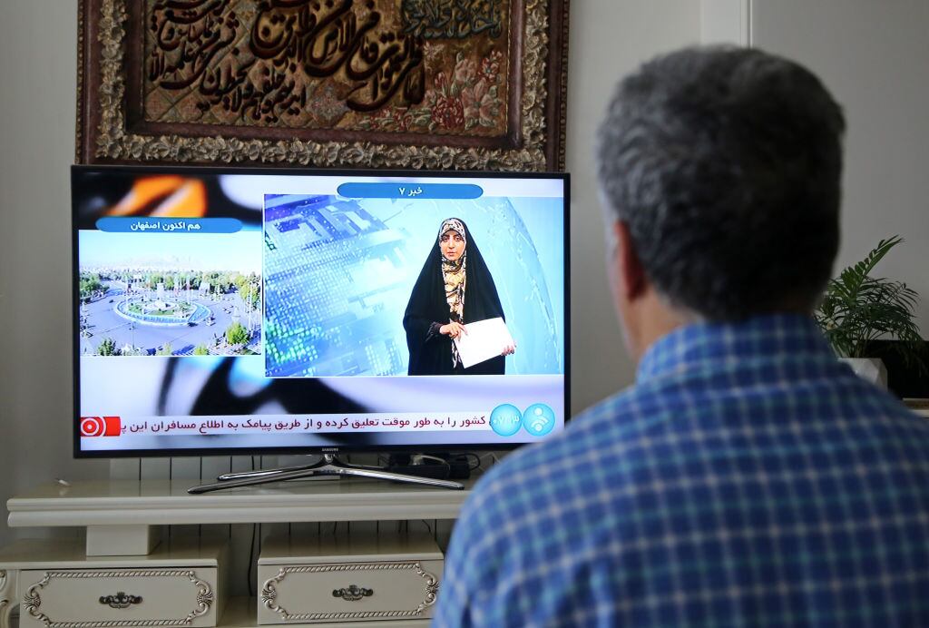 Hombre mira la televisión en la ciudad de Teherán, mientras el canal reporta una "explosión masiva" en Isfahán.