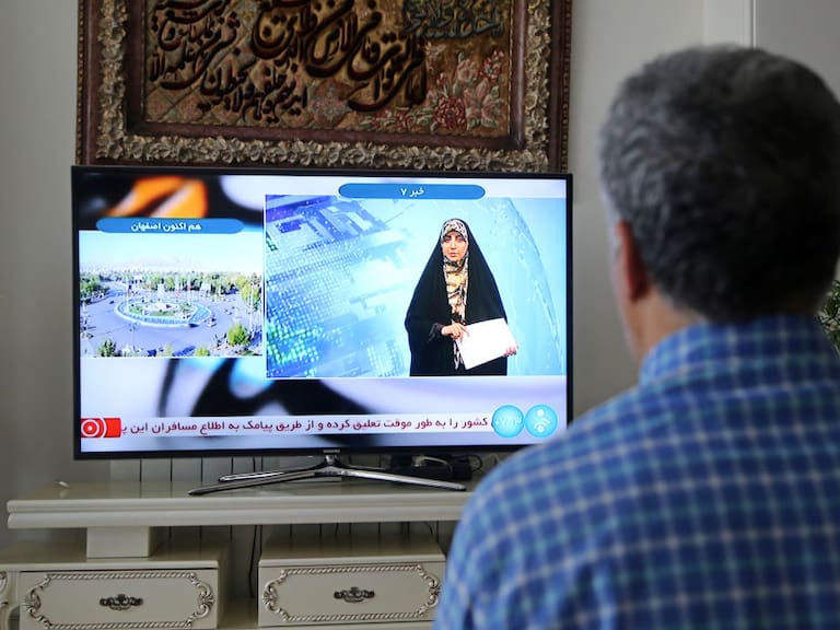 Hombre mira la televisión en la ciudad de Teherán, mientras el canal reporta una &quot;explosión masiva&quot; en Isfahán.