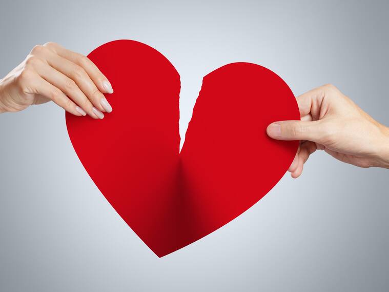 Male and female hands tearing a red heart symbol of love in half