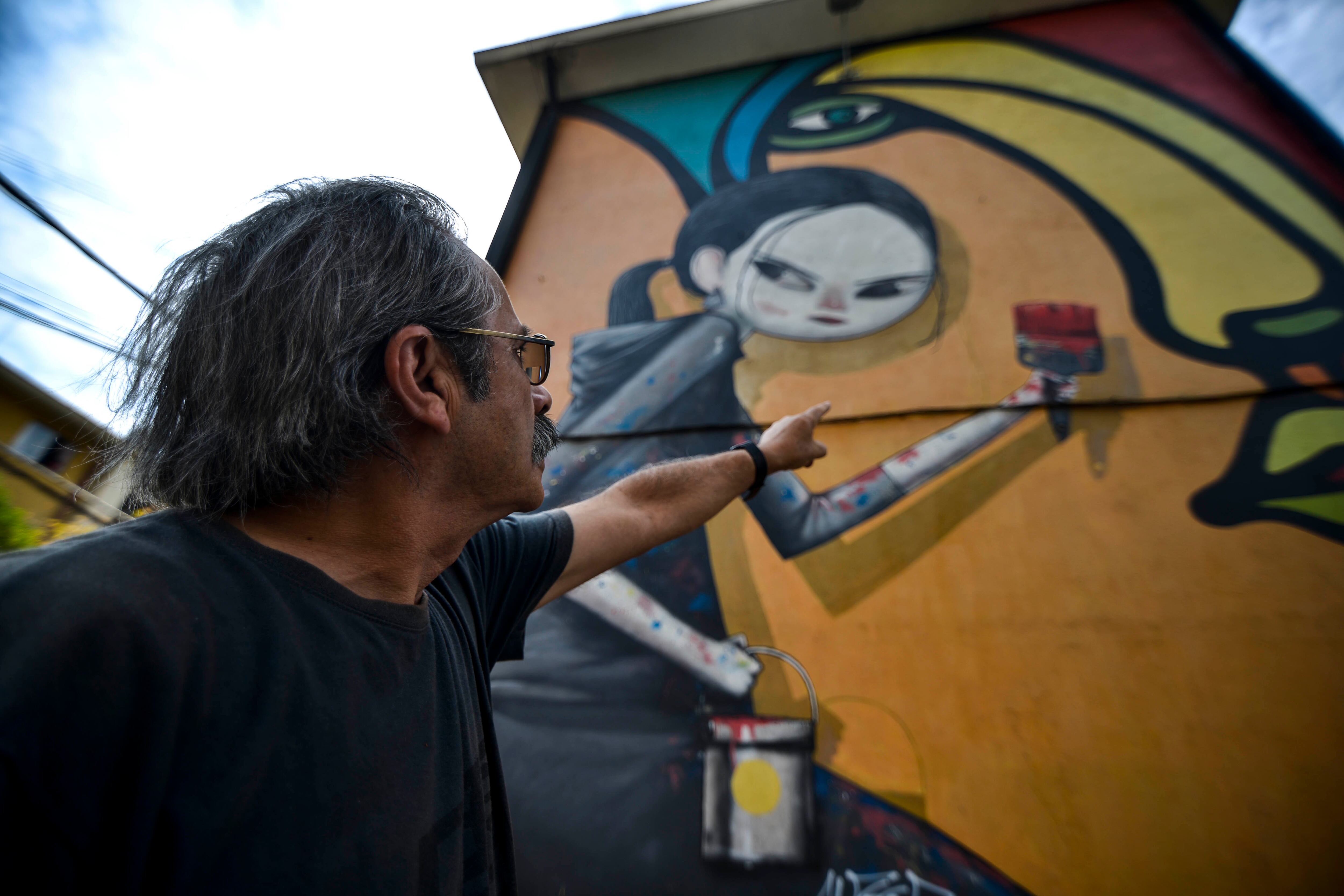 Agencia UNO | Imagen de archivo de Alejandro “Mono” González señalando una de las obras que componen el Museo a Cielo Abierto de la comuna de San Miguel.