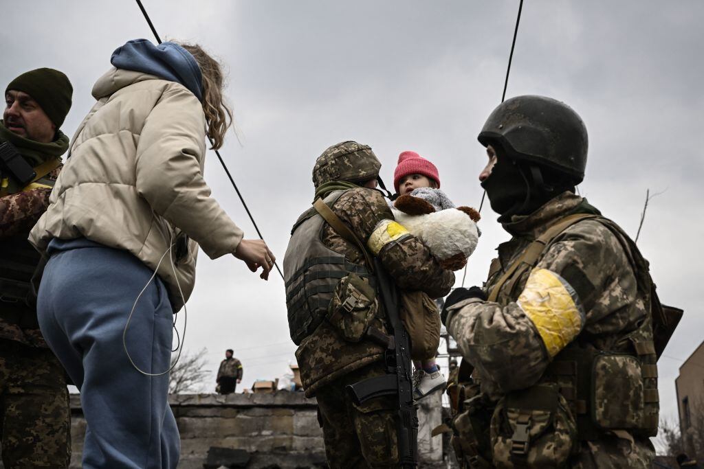Un militar ucraniano lleva a un niño mientras ayuda a las personas a cruzar un puente destruido mientras evacuan la ciudad de Irpin, al noroeste de Kiev, durante fuertes bombardeos y bombardeos el 5 de marzo de 2022, 10 días después de que Rusia lanzara una invasión militar en Ucrania. (Foto de Aris Messinis / AFP) (Foto de ARIS MESSINIS/AFP vía Getty Images)