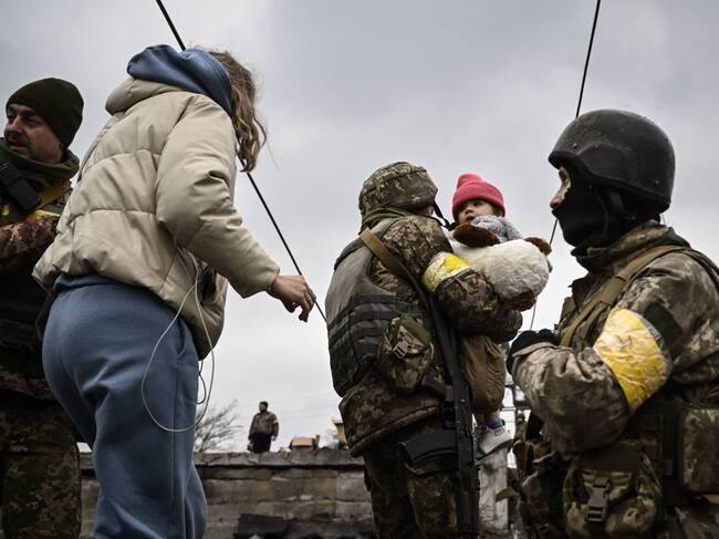 Un militar ucraniano lleva a un niño mientras ayuda a las personas a cruzar un puente destruido mientras evacuan la ciudad de Irpin, al noroeste de Kiev, durante fuertes bombardeos y bombardeos el 5 de marzo de 2022, 10 días después de que Rusia lanzara una invasión militar en Ucrania. (Foto de Aris Messinis / AFP) (Foto de ARIS MESSINIS/AFP vía Getty Images)